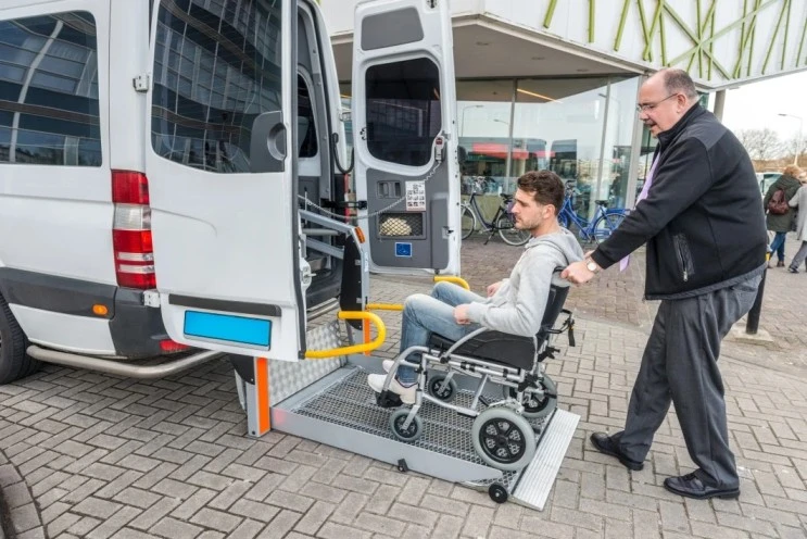 Support worker helping disabled man in wheelchair get into van